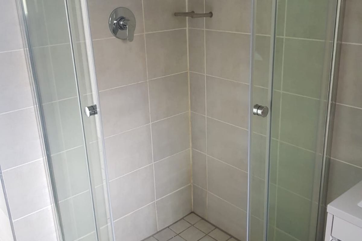 A clean, functional bathroom shower enclosure featuring neutral wall and floor tiling with a modern shower mixer and glass door entry.