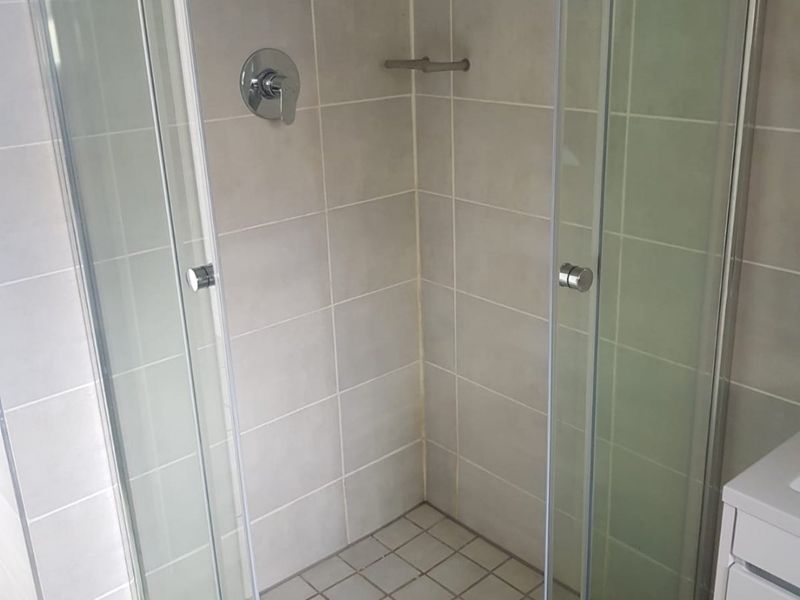 A clean, functional bathroom shower enclosure featuring neutral wall and floor tiling with a modern shower mixer and glass door entry.