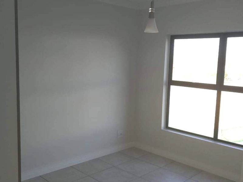 A clean, empty bedroom featuring neutral tiled flooring, a modern pendant light fixture, and a large window allowing for natural light.