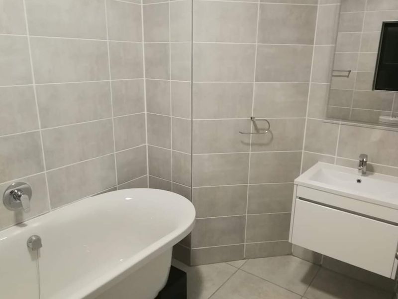 Modern bathroom featuring a freestanding bathtub, wall-mounted vanity with basin, and neutral floor-to-ceiling wall tiling.