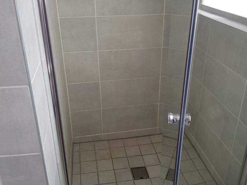 A clean, modern shower enclosure featuring neutral grey wall tiles, a tiled floor, and a glass door with chrome hardware.