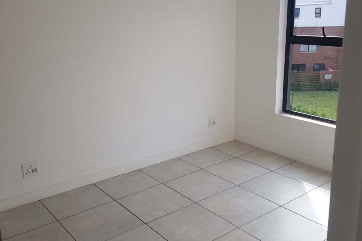A clean, empty bedroom featuring neutral tiled flooring, a modern aluminium window frame, and a simple pendant light fixture.