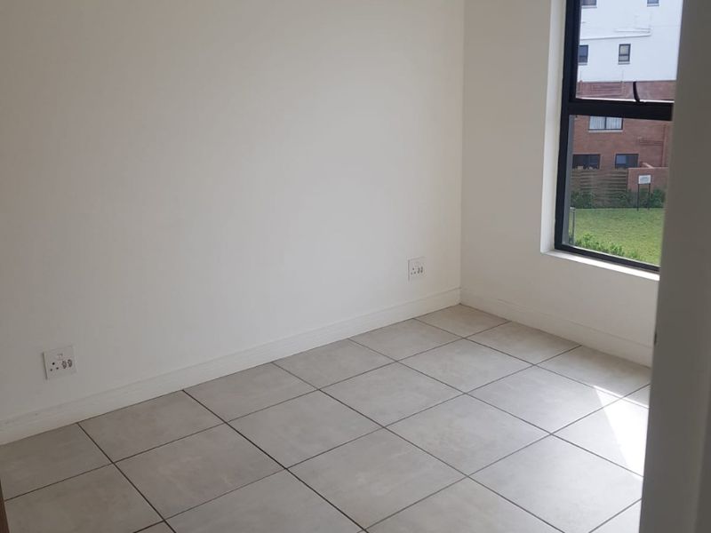 A clean, empty bedroom featuring neutral tiled flooring, a modern aluminium window frame, and a simple pendant light fixture.
