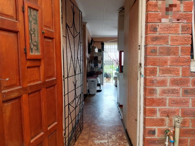 A narrow hallway entrance featuring a timber door, security gate, and exposed brickwork, showing signs of wear and requiring maintenance.