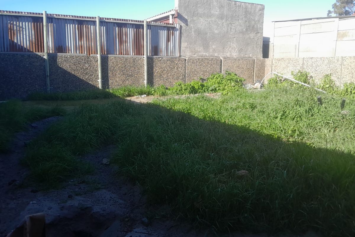A rear garden area featuring a precast concrete boundary wall and corrugated metal fencing, currently requiring significant landscaping and maintenance.