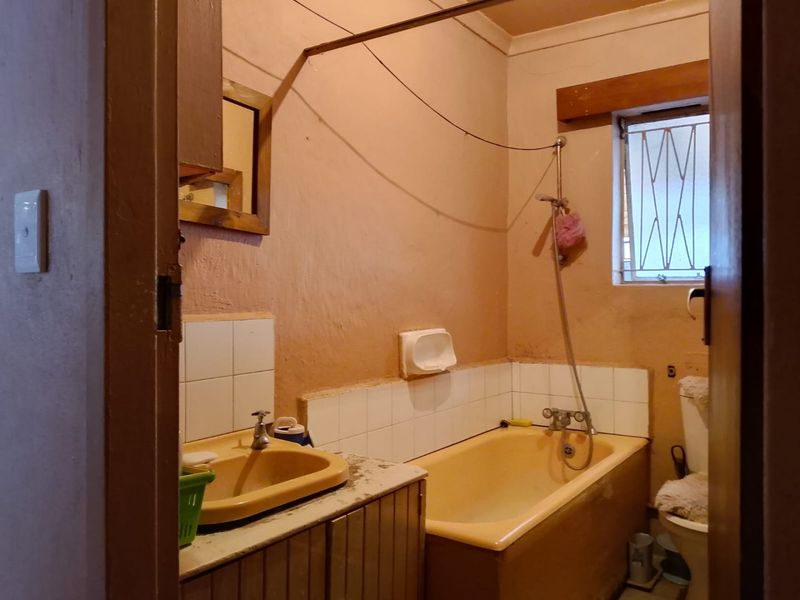 A dated bathroom featuring a built-in vanity, bathtub, and toilet, requiring modernization of finishes and fixtures to improve overall appeal and functionality.