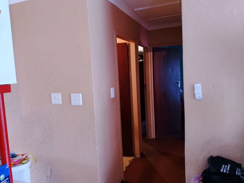 A narrow interior hallway featuring plain painted walls, multiple doorways, and standard electrical fixtures, showing signs of wear and tear.