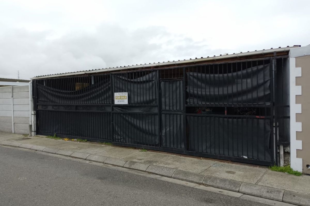 Street-facing view of the property featuring a large metal security gate and boundary wall with a for sale sign.