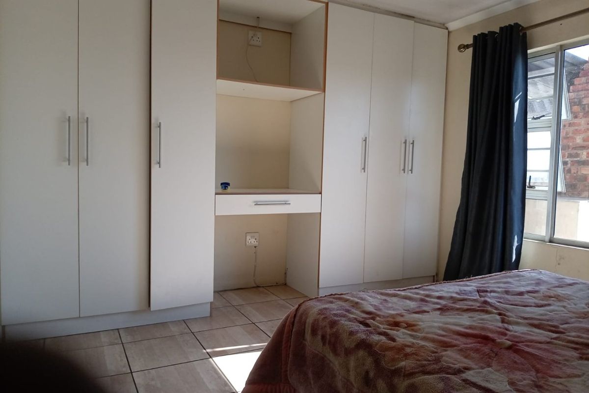 A bedroom featuring white built-in cupboards with an integrated desk area and tiled flooring.