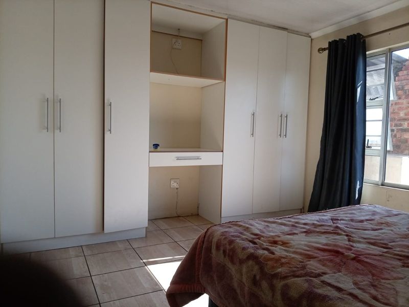 A bedroom featuring white built-in cupboards with an integrated desk area and tiled flooring.
