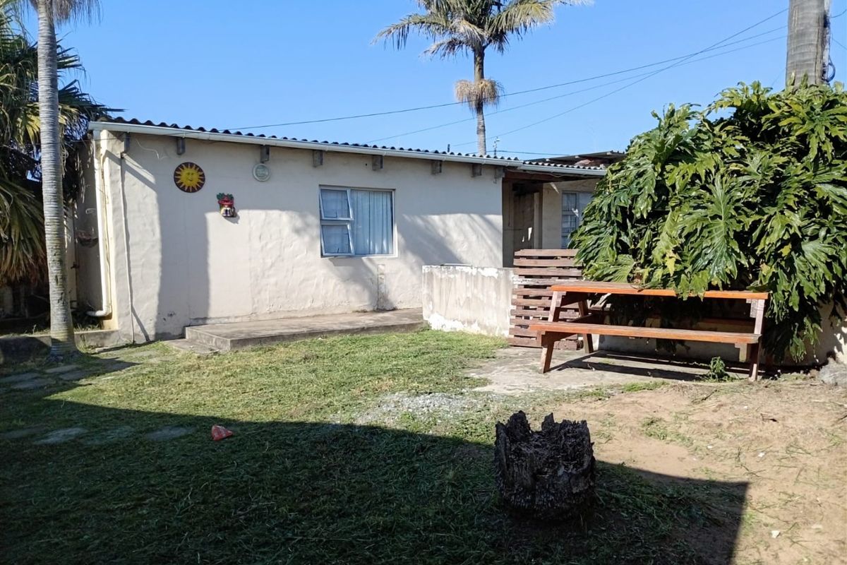 Rear view of the property featuring a small concrete patio area, lawn, and established garden foliage.