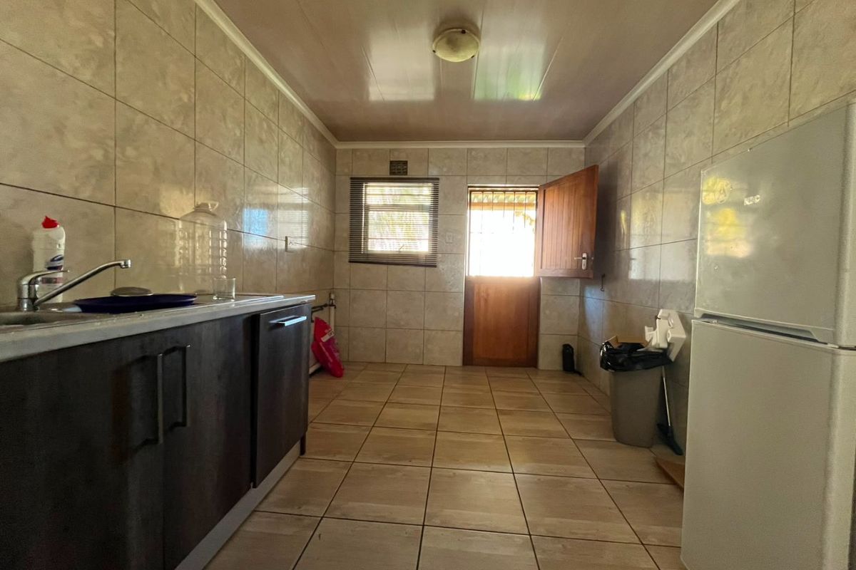 A functional kitchen space featuring tiled walls and flooring, dark cabinetry, and direct access to the exterior via a security door.