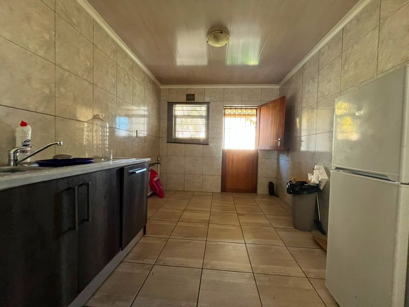 A functional kitchen space featuring tiled walls and flooring, dark cabinetry, and direct access to the exterior via a security door.
