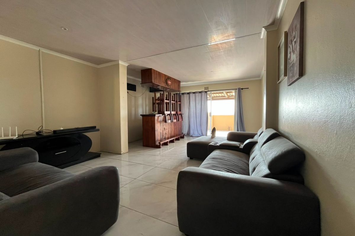Spacious living room featuring tiled flooring and a built-in wooden bar, with direct access to an outdoor patio area through sliding glass doors.