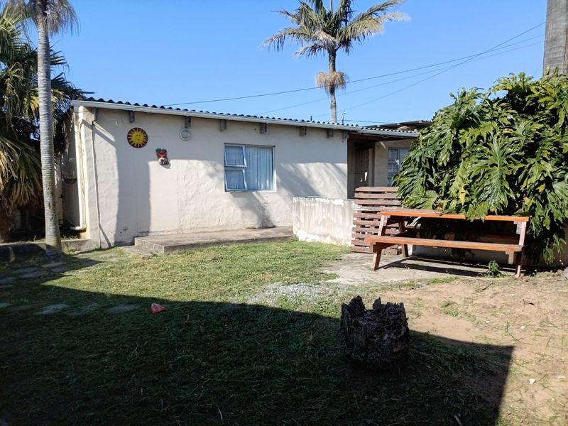 Rear view of the property featuring a small concrete patio, lawn area, and low masonry wall boundary.