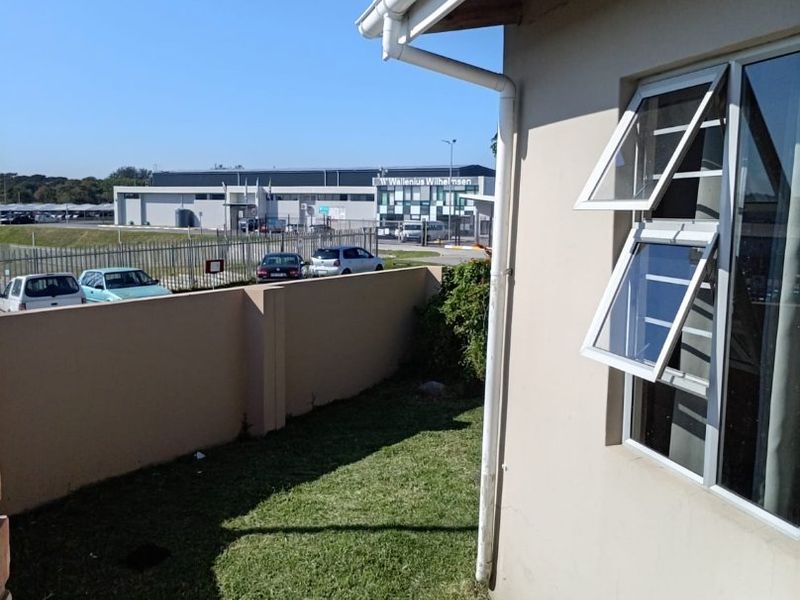 A view of the rear exterior area featuring a perimeter wall, lawn, and top-hung window frames.