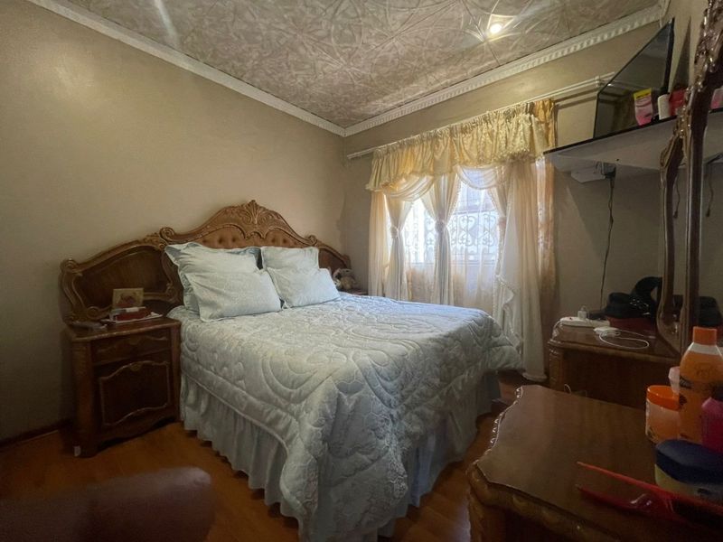 A bedroom featuring laminate flooring, decorative ceiling tiles, and crown molding, with security bars installed on the window.