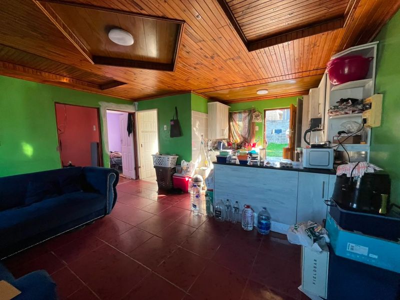 Open plan living and kitchen area featuring timber panelled ceilings and tiled flooring, requiring cosmetic updates to finishes and wall surfaces.