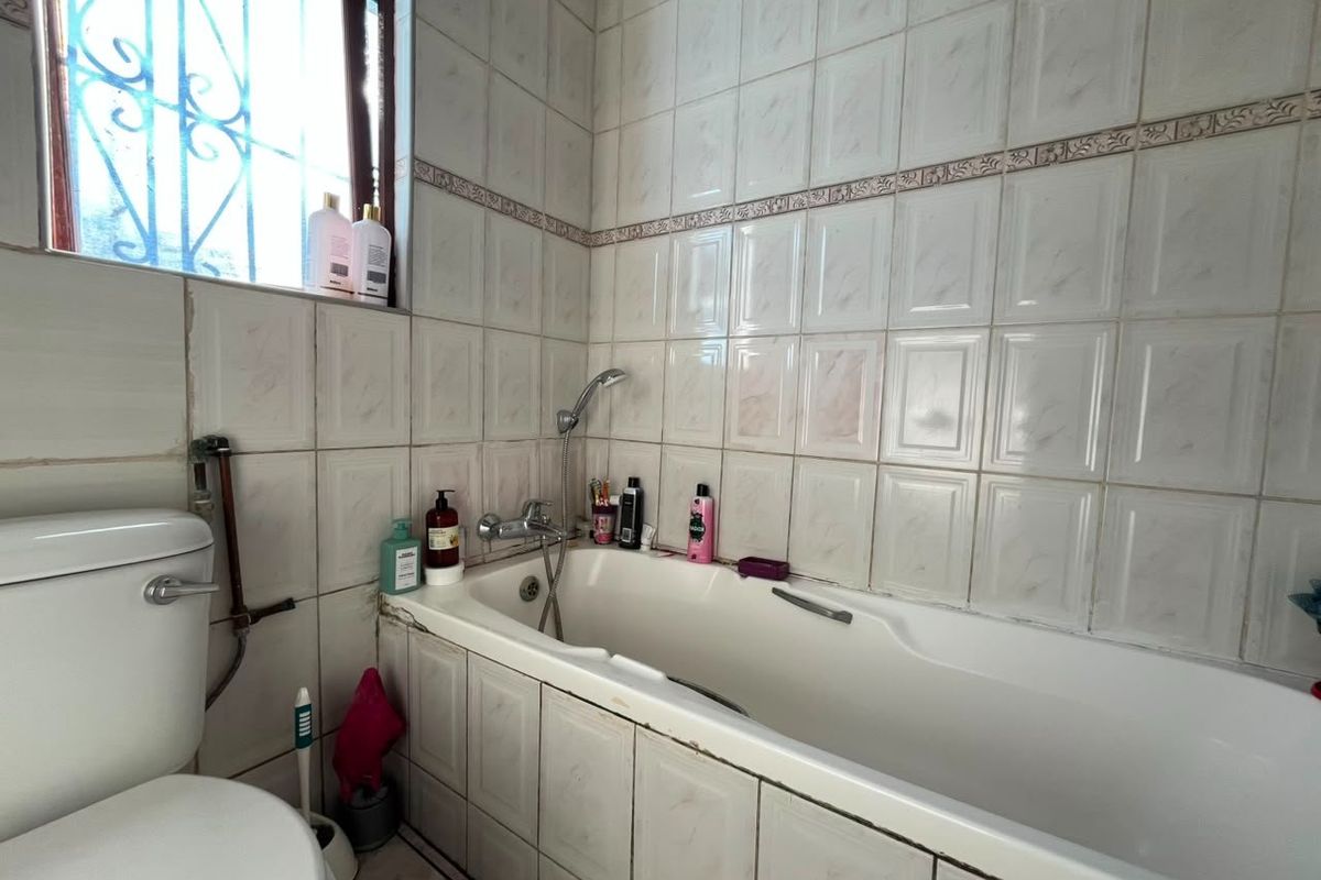 A functional bathroom featuring a standard bathtub with shower mixer, toilet, and tiled wall finishes.