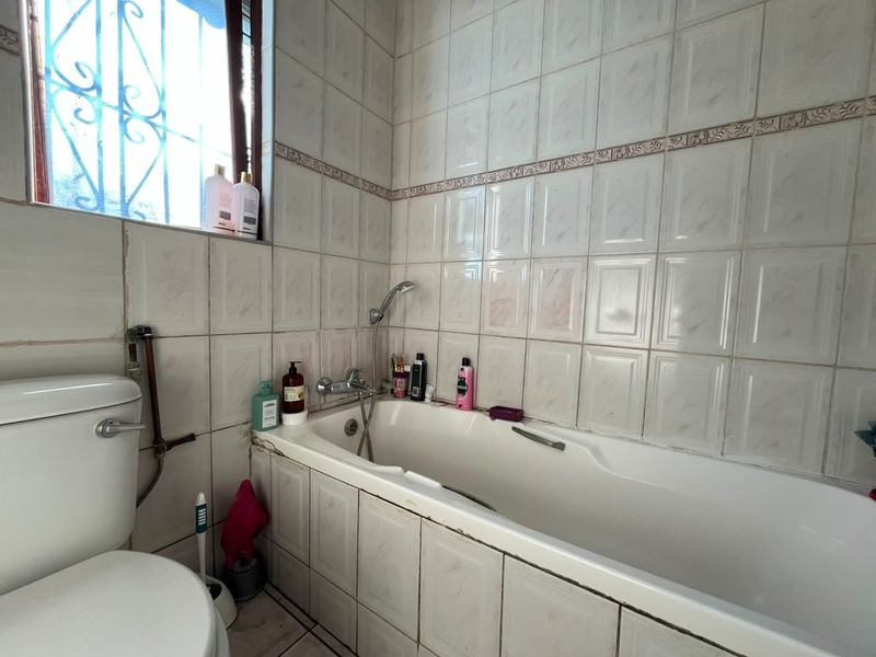 A functional bathroom featuring a standard bathtub with shower mixer, toilet, and tiled wall finishes.