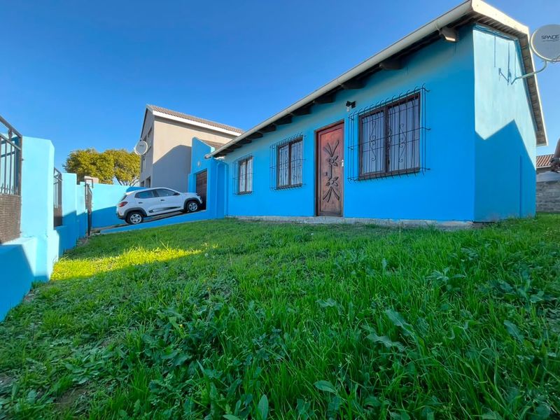 Front exterior view of a blue house featuring security bars on windows, a timber entrance door, and a concrete driveway.