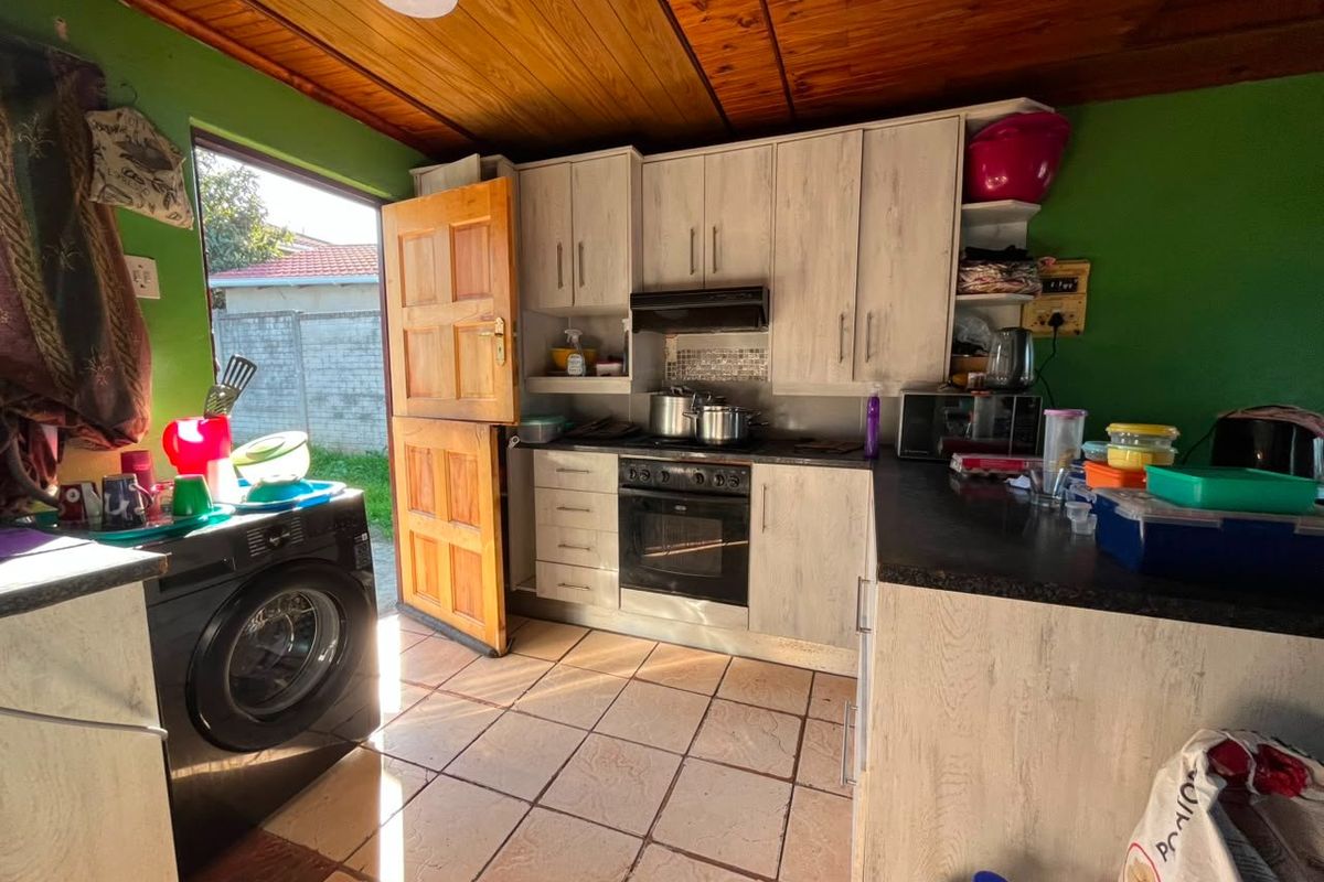 A functional kitchen featuring built-in cabinetry, integrated oven and hob, tiled flooring, and a timber ceiling with direct access to the rear exterior.