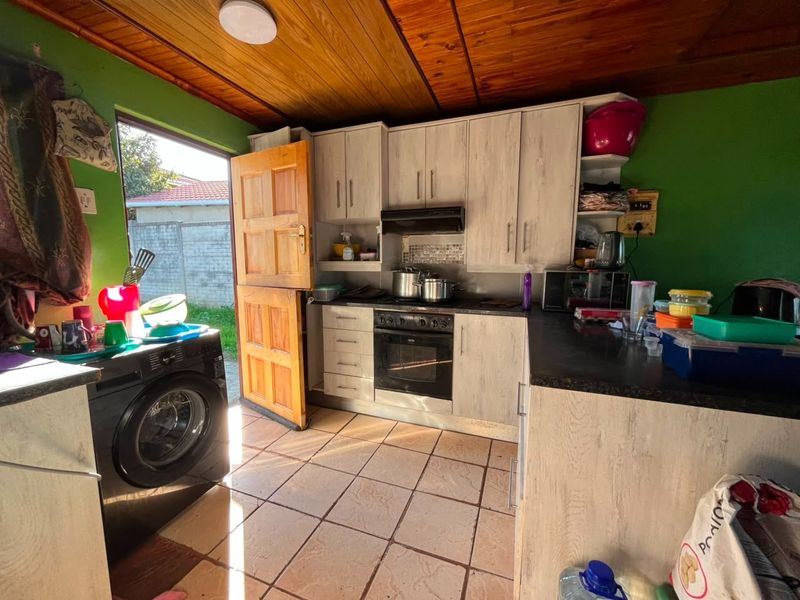 A functional kitchen featuring built-in cabinetry, integrated oven and hob, tiled flooring, and a timber ceiling with direct access to the rear exterior.