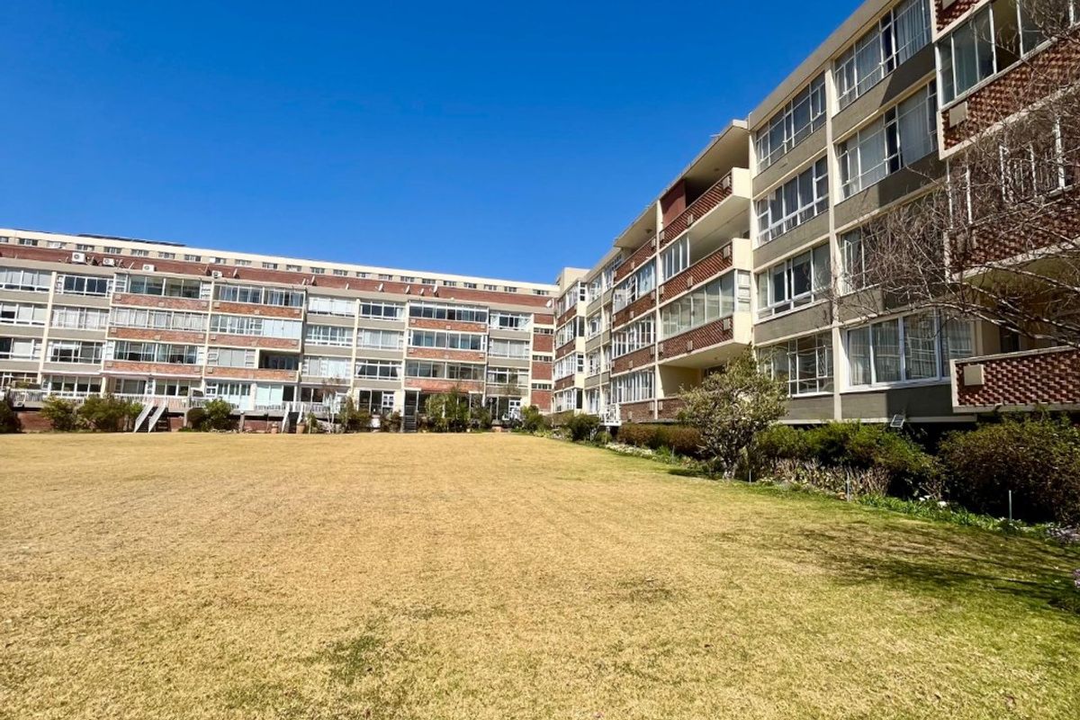 A wide-angle view of the rear facade of a multi-story apartment complex featuring private balconies overlooking a large, open communal lawn area.