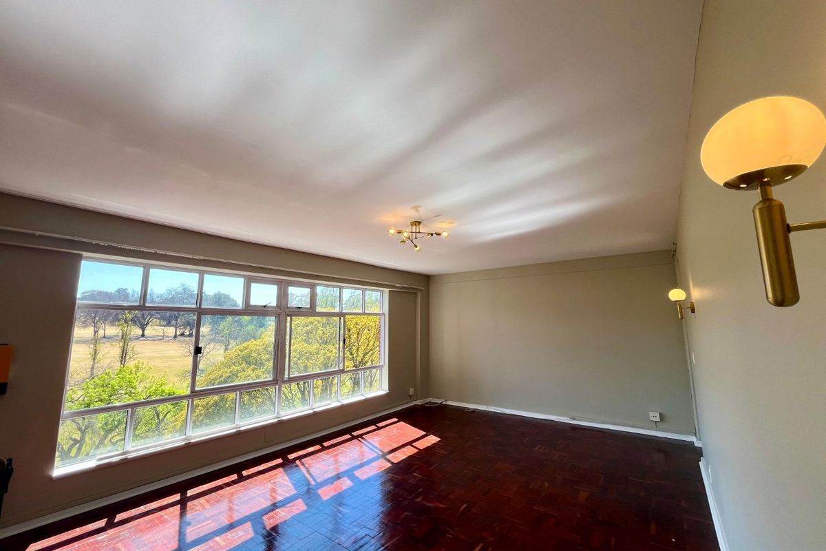 Spacious living room featuring polished parquet flooring, large windows with scenic views, and modern wall-mounted lighting fixtures.