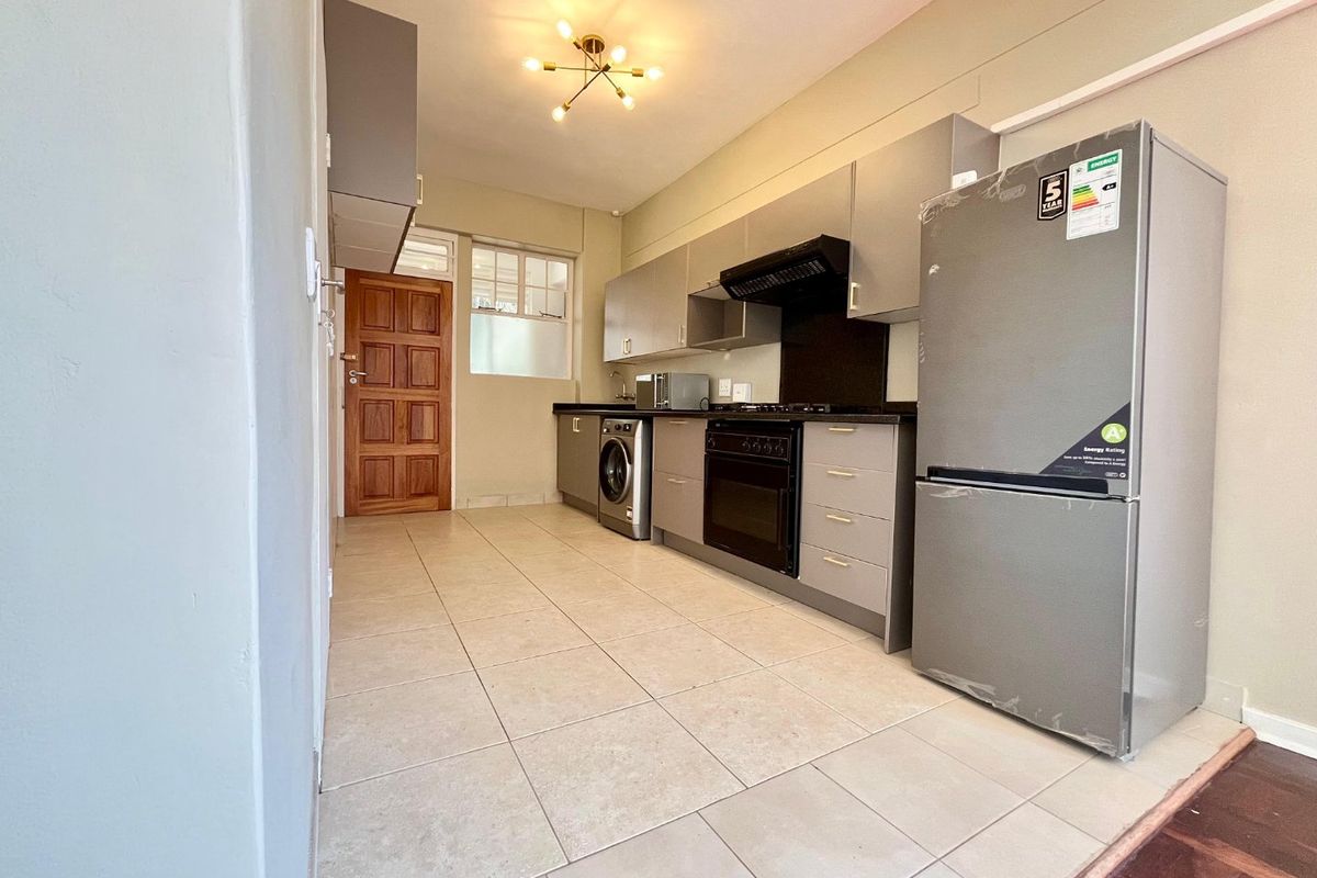 A functional kitchen featuring modern grey cabinetry, built-in oven and hob, extractor fan, and tiled flooring, with direct access to an exterior door.