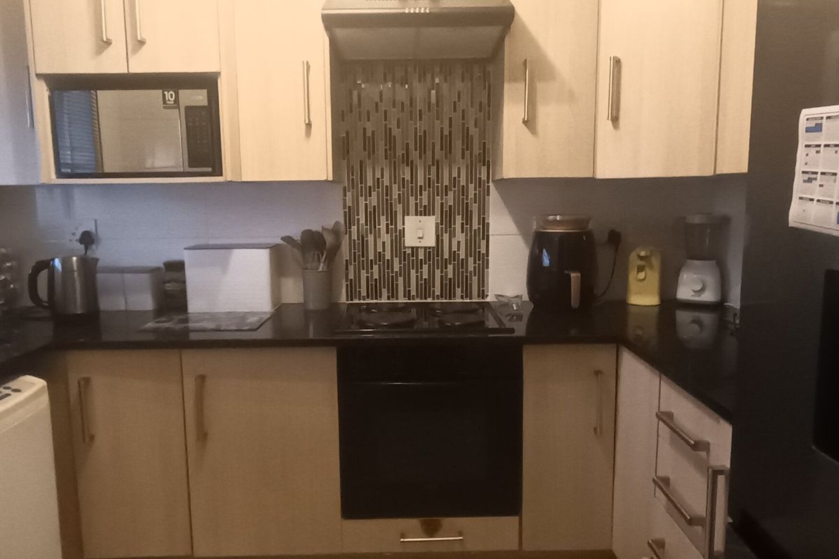 A functional kitchen featuring light-toned cabinetry, black granite countertops, a mosaic tile splashback, and integrated appliances including an oven, hob, and extractor fan.