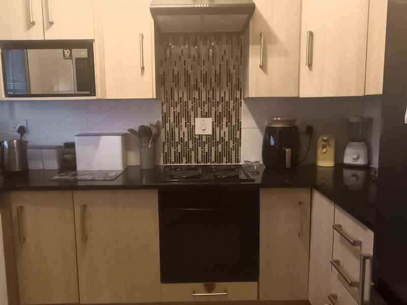 A functional kitchen featuring light-toned cabinetry, black granite countertops, a mosaic tile splashback, and integrated appliances including an oven, hob, and extractor fan.