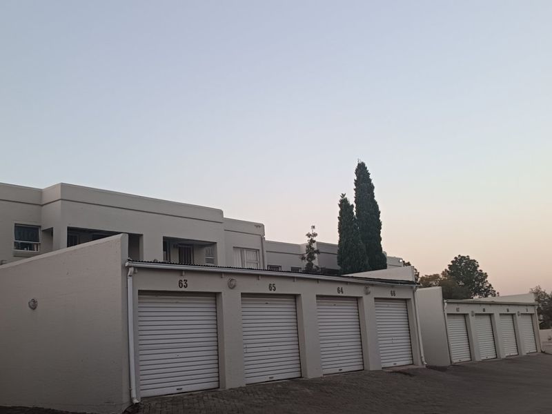 Exterior view of an apartment complex featuring a row of secure, roller shutter garage units and paved driveway access.