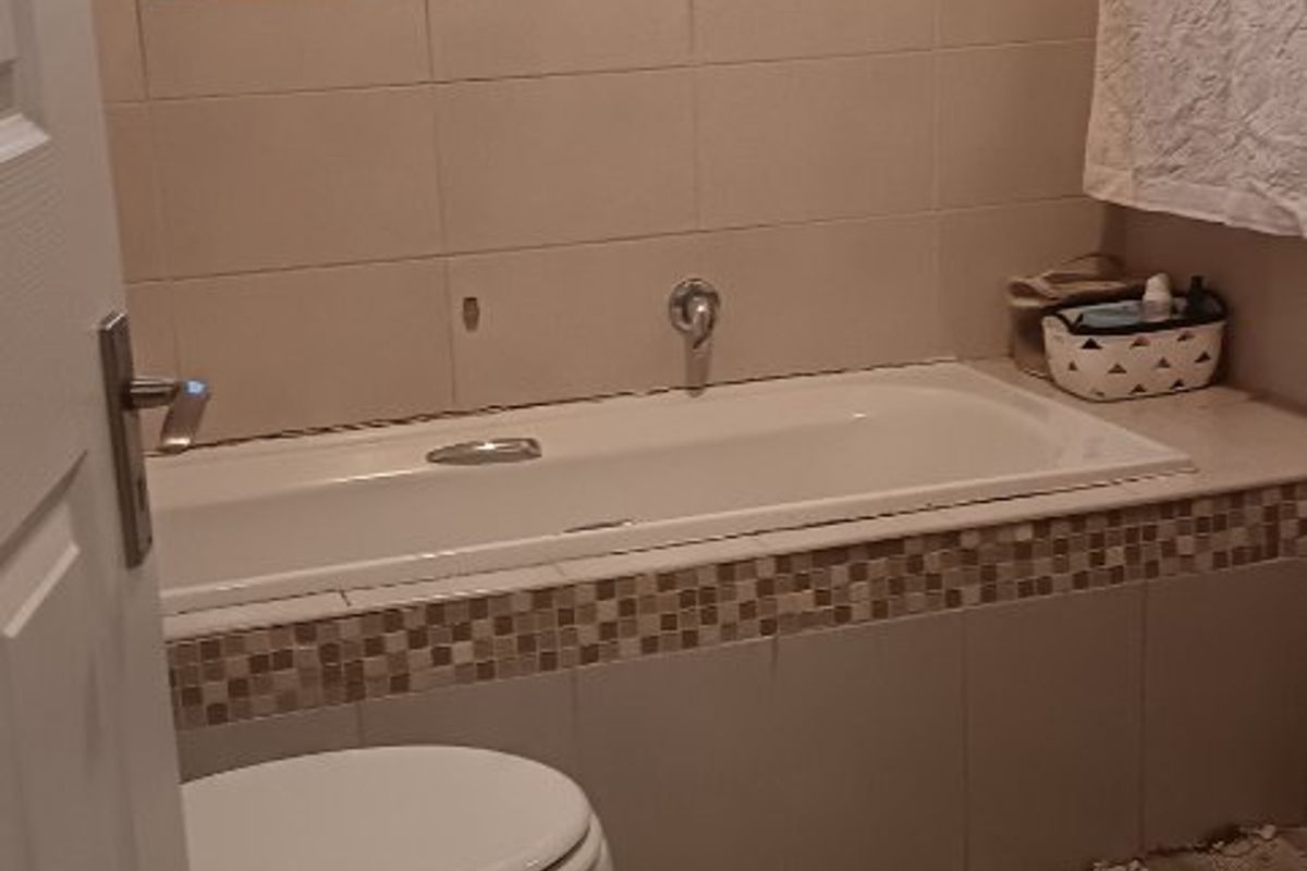 A functional bathroom featuring a built-in bathtub, toilet, and neutral wall and floor tiling with decorative mosaic accents.
