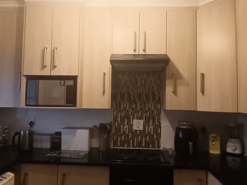 A functional kitchen featuring light wood-tone cabinetry, dark countertops, a mosaic tile splashback, and a built-in extractor fan.
