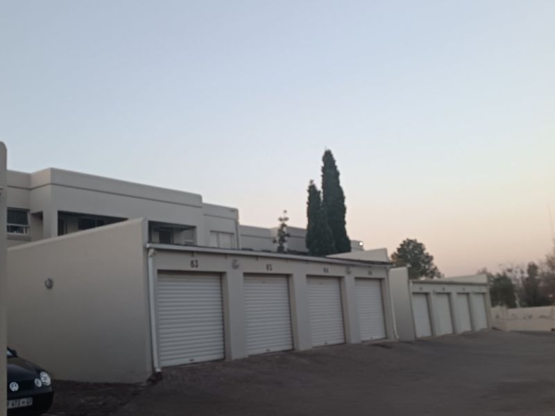 Exterior view of an apartment complex featuring a row of roller shutter garage doors and a paved driveway area.