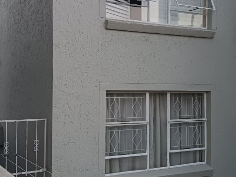 Rear exterior view of the apartment building featuring textured plaster walls, security-barred windows, and a small garden area.