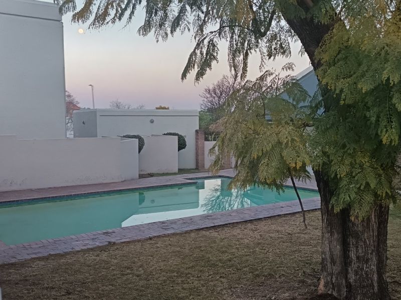 Outdoor pool area featuring a swimming pool with brick coping, surrounding boundary walls, and a built-in braai area in a garden setting.