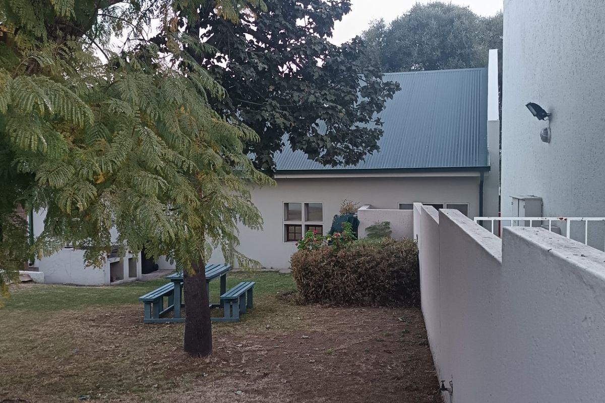 A view of the rear garden area featuring a boundary wall, metal railing, and a built-in braai facility.