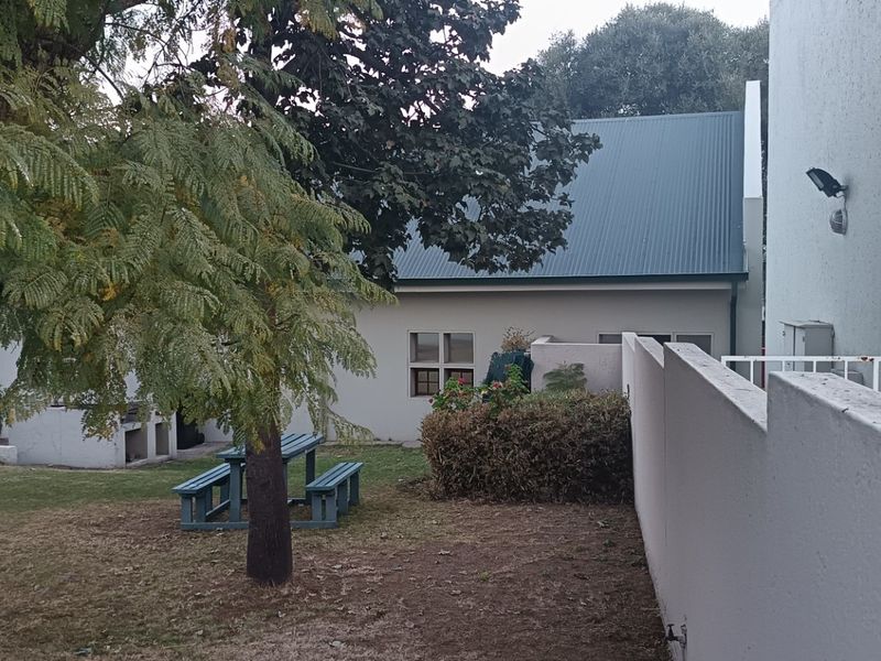 A view of the rear garden area featuring a boundary wall, metal railing, and a built-in braai facility.