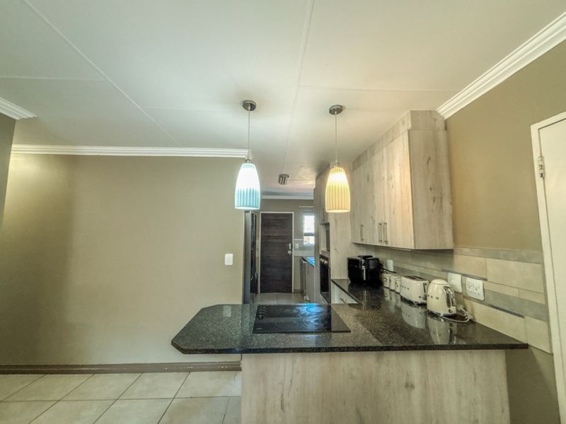 A functional kitchen featuring granite countertops, light wood-finish cabinetry, an integrated electric hob, and modern pendant lighting, with tiled flooring throughout.