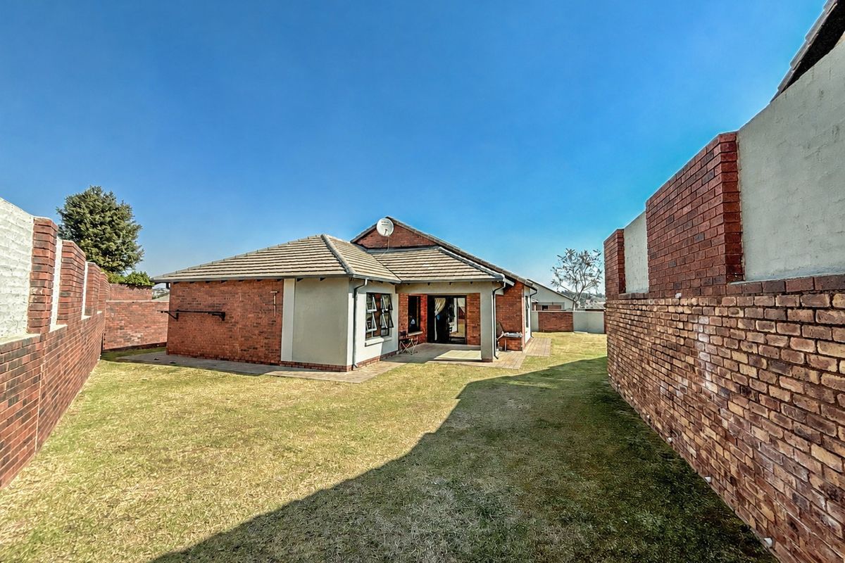 Rear view of the townhouse featuring a private garden, brick boundary walls, a paved patio area, and a tiled roof.