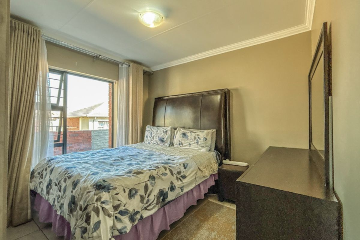 A functional bedroom featuring tiled flooring, ceiling cornice detailing, and a sliding window providing natural light.