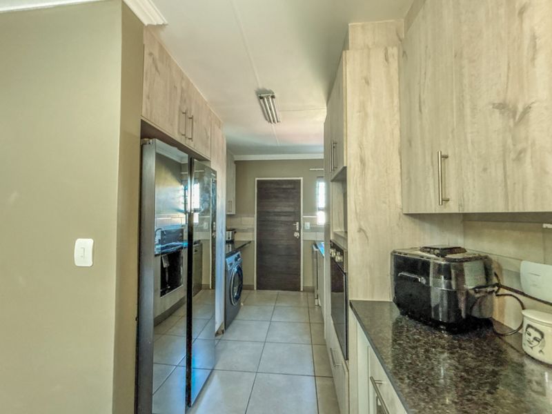 A functional scullery featuring light wood-grain cabinetry, granite countertops, tiled flooring, and a built-in oven, providing additional prep and storage space.