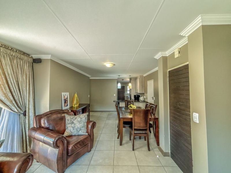 An open-plan living and dining area featuring neutral wall tones, tiled flooring, crown molding, and a seamless transition into the kitchen space.