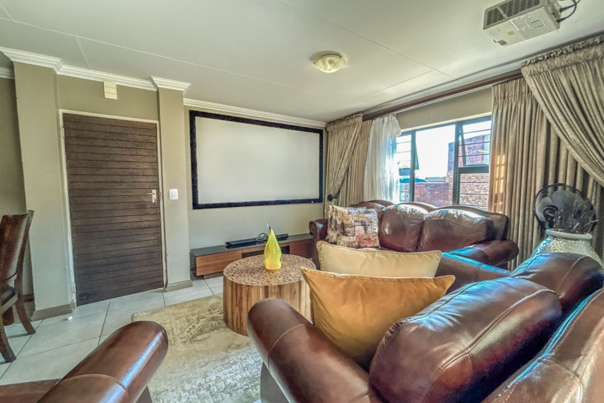 A living room featuring a built-in projector screen and ceiling-mounted projector, finished with tiled flooring and decorative cornicing.
