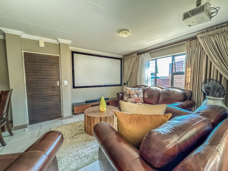 A living room featuring a built-in projector screen and ceiling-mounted projector, finished with tiled flooring and decorative cornicing.