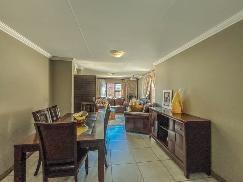An open-plan living and dining area featuring neutral wall tones, tiled flooring, and decorative ceiling cornicing, providing a functional and connected living space.