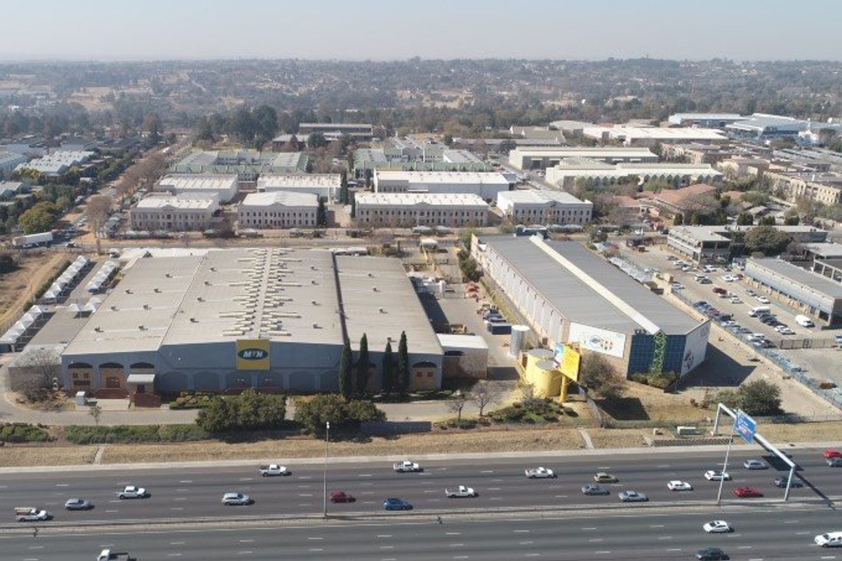 Aerial view of an industrial park complex featuring large warehouse facilities, paved parking, and direct access to a major highway.