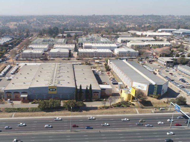 Aerial view of an industrial park complex featuring large warehouse facilities, paved parking, and direct access to a major highway.